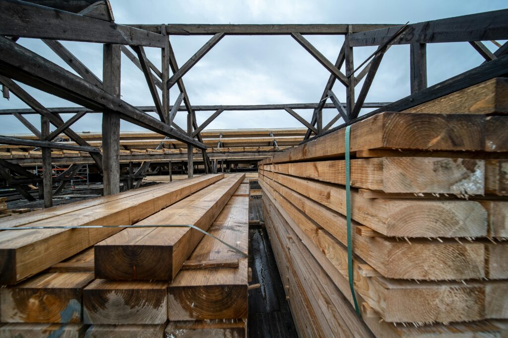 Stacked timber planks in an outdoor industrial storage area under a cloudy sky.