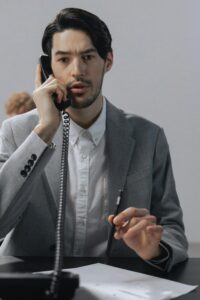 Focused young man in a gray suit conversing on telephone at an office desk.